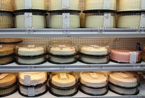 A display of various cakes in clear plastic containers on a supermarket shelf.