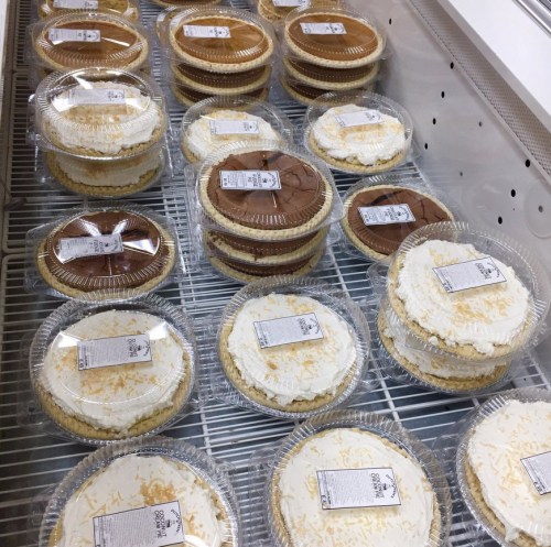 A display of various cakes in clear containers, each labeled, arranged neatly in a refrigerated case.