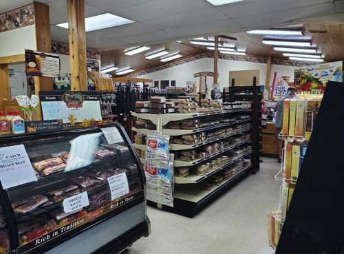 Interior of a grocery store featuring shelves of snacks, meats, and cheeses, with a display case in the foreground.
