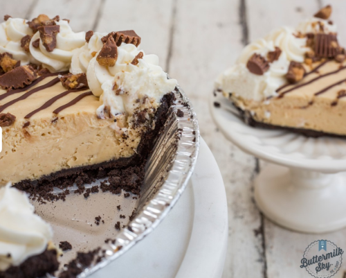 A creamy peanut butter pie with whipped cream and chocolate drizzle, served on a white pedestal.