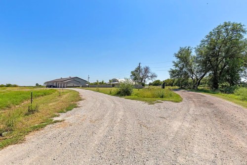 A gravel road splits into two paths, with a building and trees in the background under a clear blue sky.