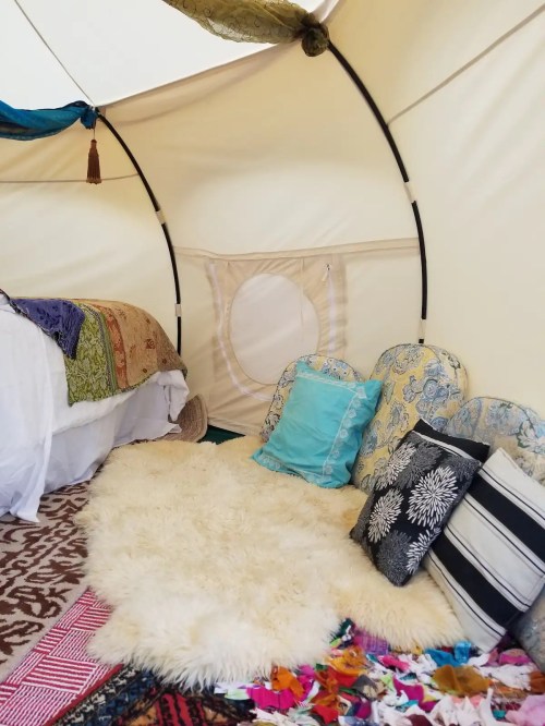 Cozy interior of a tent with a bed, colorful cushions, and a soft rug, creating a warm, inviting atmosphere.
