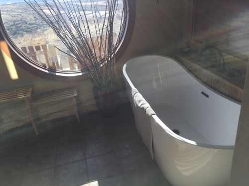 A modern bathroom featuring a freestanding tub, large round window, and natural light streaming in.