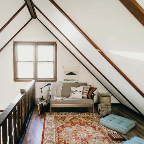 Cozy attic space with sloped ceilings, a rug, a sofa, and a small seating area by the window.