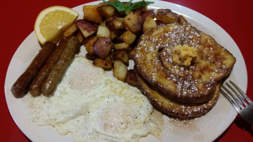 A plate of breakfast featuring French toast, eggs, sausage, and seasoned potatoes, garnished with lemon and mint.