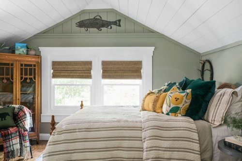 Cozy bedroom with green walls, a bed with striped bedding, decorative pillows, and a fish art piece above the windows.
