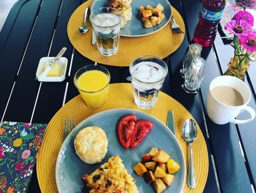 A beautifully set breakfast table with two plates of food, drinks, and colorful flowers on a black table.
