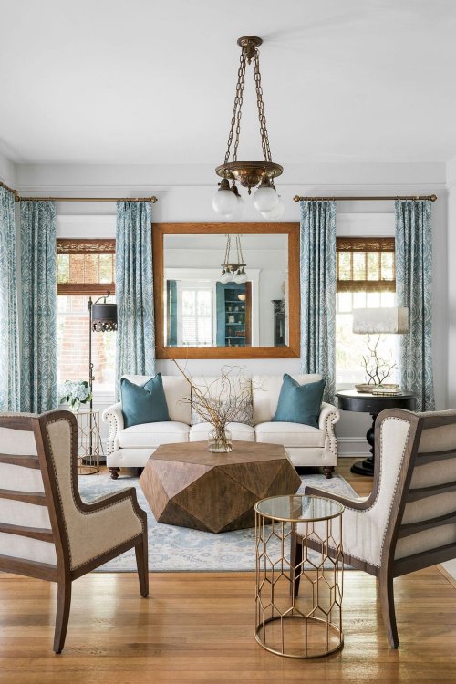 A cozy living room with a white sofa, blue accents, a geometric coffee table, and elegant curtains.