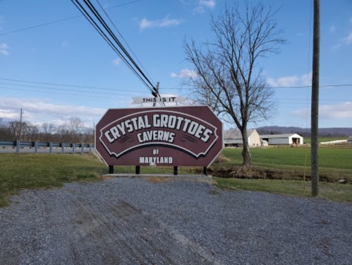 Sign for Crystal Grottoes Caverns of Maryland, set against a blue sky and grassy landscape.