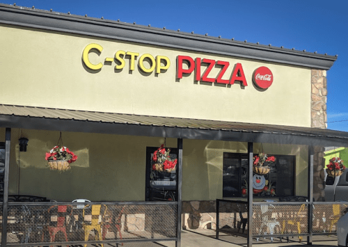Exterior of C-Stop Pizza restaurant with colorful signage and hanging flower baskets.