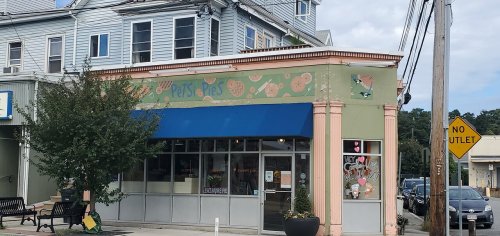 A colorful storefront of a pet shop with a blue awning, surrounded by trees and a street sign indicating no outlet.