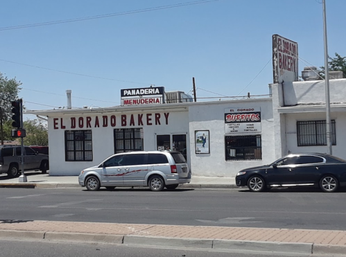 A bakery building with "El Dorado Bakery" sign, featuring a menu board and cars passing by on the street.