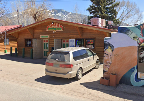 A wooden building with a sign reading "Mafe's Cantina y Cocina," parked van, and colorful mural on the side.