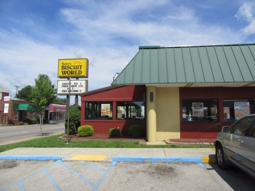 Exterior of a restaurant called "Biscuit World," featuring a green roof and a sign with menu items. Clear blue sky above.