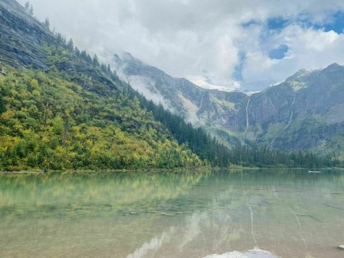 A serene lake surrounded by lush green mountains and mist, reflecting the landscape in calm waters.
