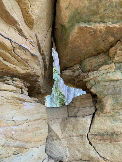 A narrow gap between two large rock formations, revealing trees in the background.