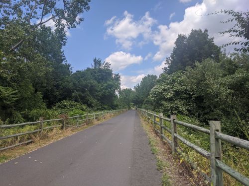 A paved path surrounded by lush greenery and trees under a partly cloudy sky.
