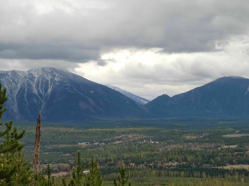 A scenic view of mountains under a cloudy sky, with a forested valley in the foreground.