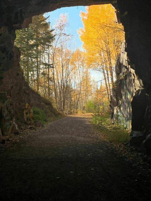 A view through a rocky archway, revealing a path lined with autumn trees and bright yellow leaves.