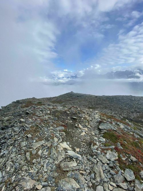 A rocky mountain ridge under a cloudy sky, with mist and distant peaks partially visible.