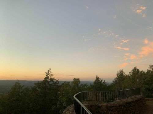 A serene landscape at sunset, featuring a curved railing and trees against a colorful sky.