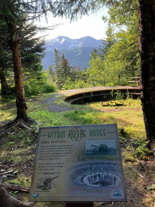 A scenic view of mountains and trees, with a sign about Coast Artillery and historical context in the foreground.