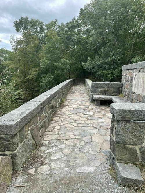 A stone pathway leads through a lush green landscape, flanked by low stone walls on either side.