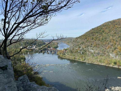 Scenic view of a river winding through hills, with trees and a small town visible in the distance under a clear sky.
