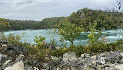 A scenic view of a river surrounded by lush greenery and rocky terrain under a cloudy sky.