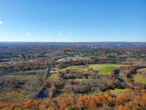 A panoramic view of a colorful autumn landscape with rolling hills, trees, and a clear blue sky.