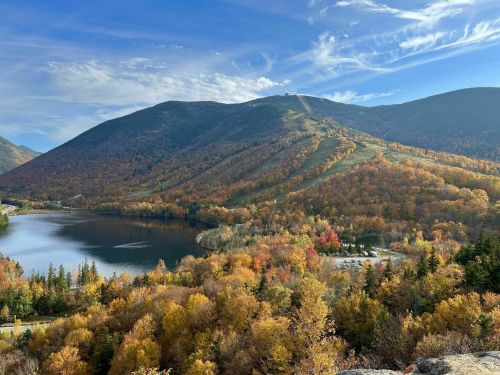 A scenic view of mountains and a lake surrounded by vibrant autumn foliage under a clear blue sky.