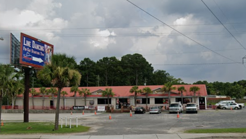 A building with a red roof and palm trees, featuring a sign for line dancing, under a cloudy sky.