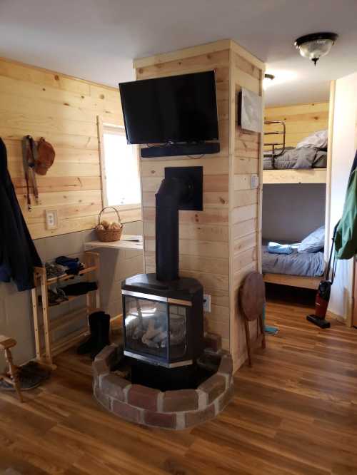 Cozy interior of a small cabin featuring a wood stove, TV, and bunk beds with wooden walls and flooring.