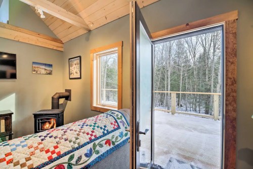 Cozy interior with a quilted blanket, open door revealing a snowy outdoor deck and forest view.