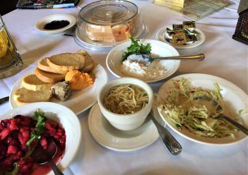 A table spread with various dishes, including bread, salads, noodles, and desserts, arranged on white plates.