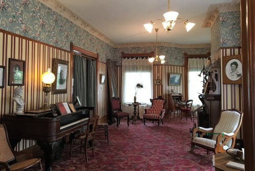 A vintage parlor with patterned wallpaper, a piano, elegant furniture, and soft lighting, evoking a classic atmosphere.