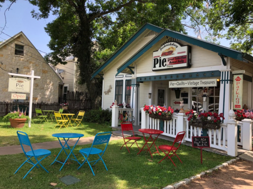 Charming pie shop with colorful outdoor seating, flowers, and a welcoming sign, set in a quaint neighborhood.