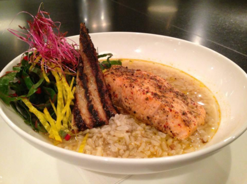 A bowl of rice topped with seasoned salmon, greens, and crispy garnishes, served in a rich broth.