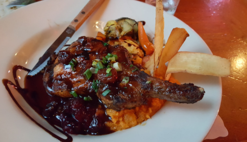 A plate featuring grilled chicken with a rich sauce, served with mashed sweet potatoes, grilled vegetables, and fries.