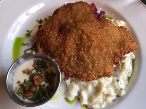 Crispy fried chicken on a bed of creamy potato salad, garnished with herbs and a side of dipping sauce.