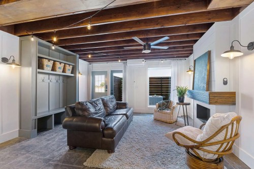 Cozy living room with a leather sofa, wooden beams, and a modern fireplace, featuring natural light and stylish decor.