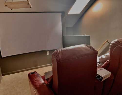 Cozy home theater with red recliners facing a large blank screen and a projector. Soft lighting enhances the ambiance.