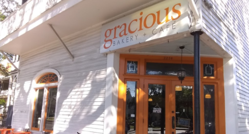 Exterior of Gracious Bakery + Cafe, featuring a light-colored wooden facade and orange accents, with an "OPEN" sign.