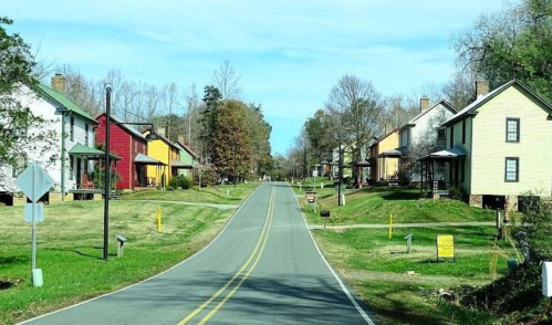 A quiet street lined with colorful houses and trees, under a clear blue sky.