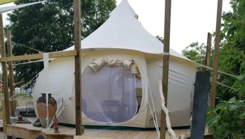 A white tent with a round entrance, set on a wooden deck surrounded by greenery.
