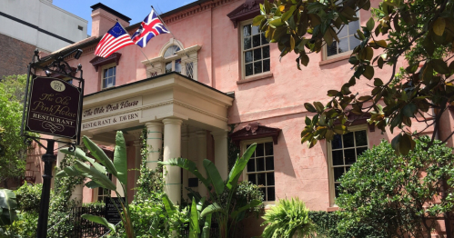 Historic pink building with American and British flags, featuring a sign for The Old Pink House restaurant and lush greenery.
