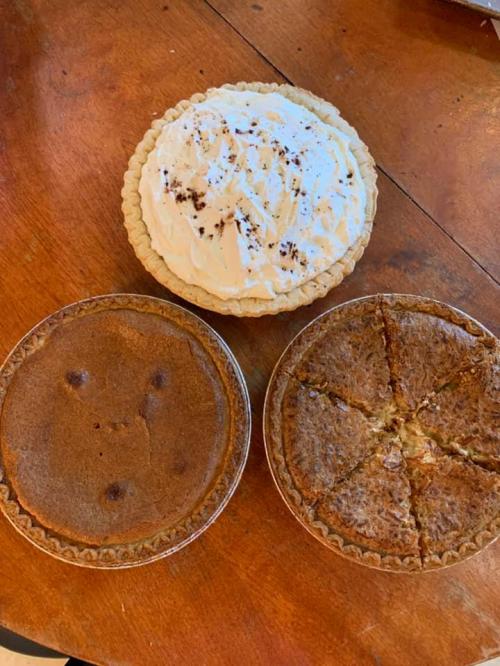 Three pies on a wooden table: a cream pie on top and two different types of baked pies below.