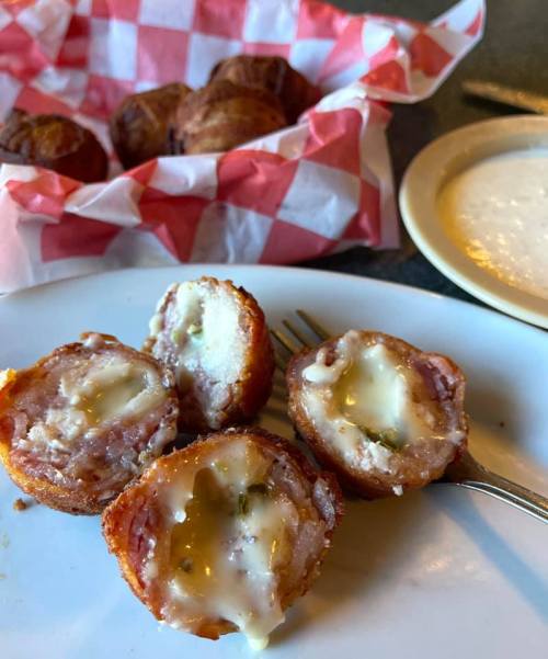 A plate with three halved, crispy cheese-stuffed balls, with a fork beside them and a basket of more in the background.