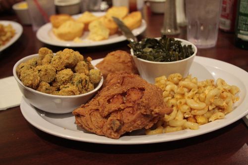 A plate of Southern comfort food featuring fried chicken, macaroni and cheese, collard greens, and fried okra.