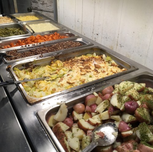 A buffet spread featuring various dishes, including green beans, carrots, potatoes, and a casserole.